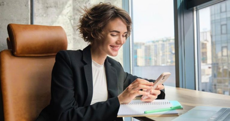 Femeie zâmbind în timp ce verifică oferta de credit aprobată pe telefonul mobil